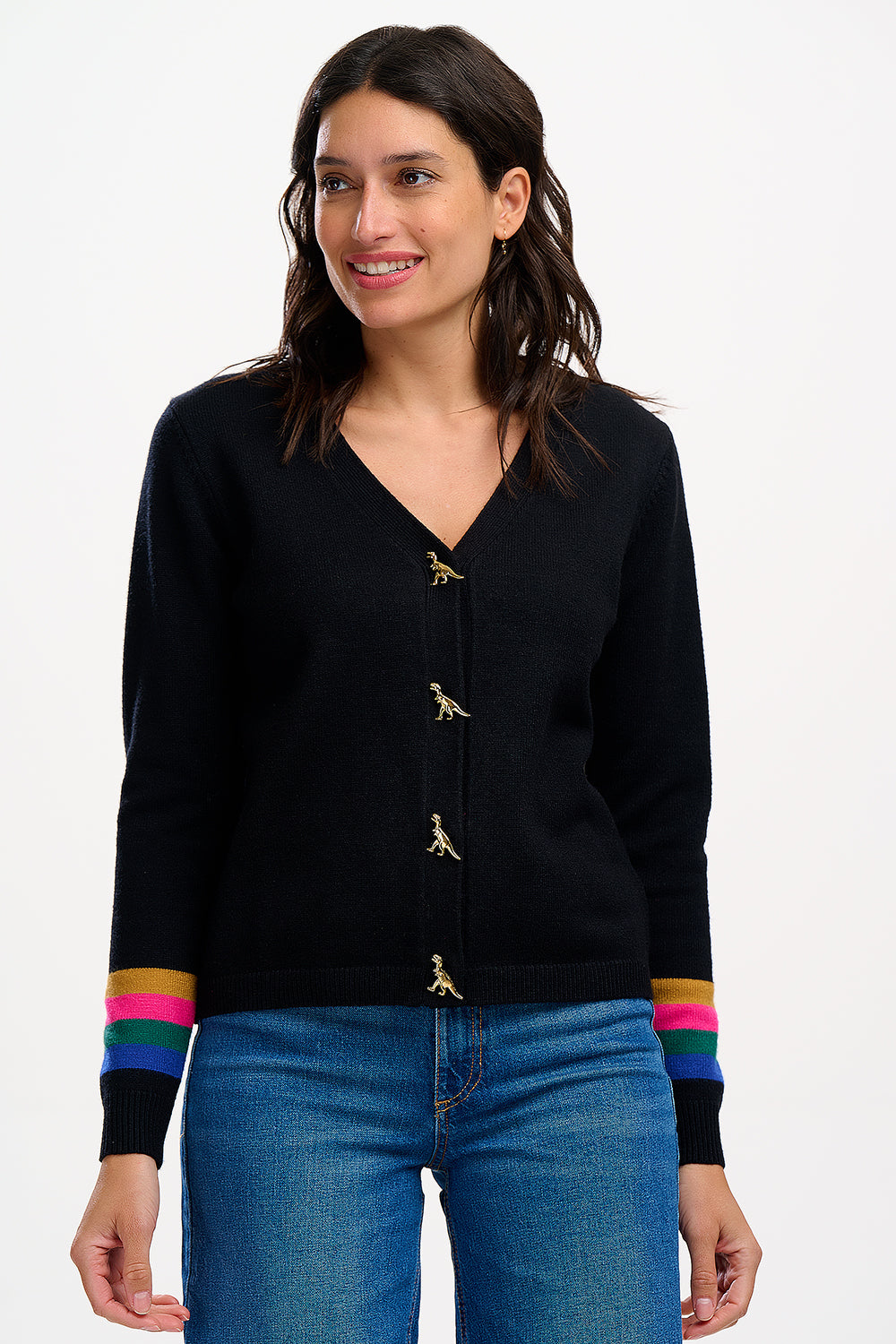 Sugarhill Brighton model wearing a black cardigan with dinosaur buttons and rainbow stripes on the cuffs, paired with blue jeans.
