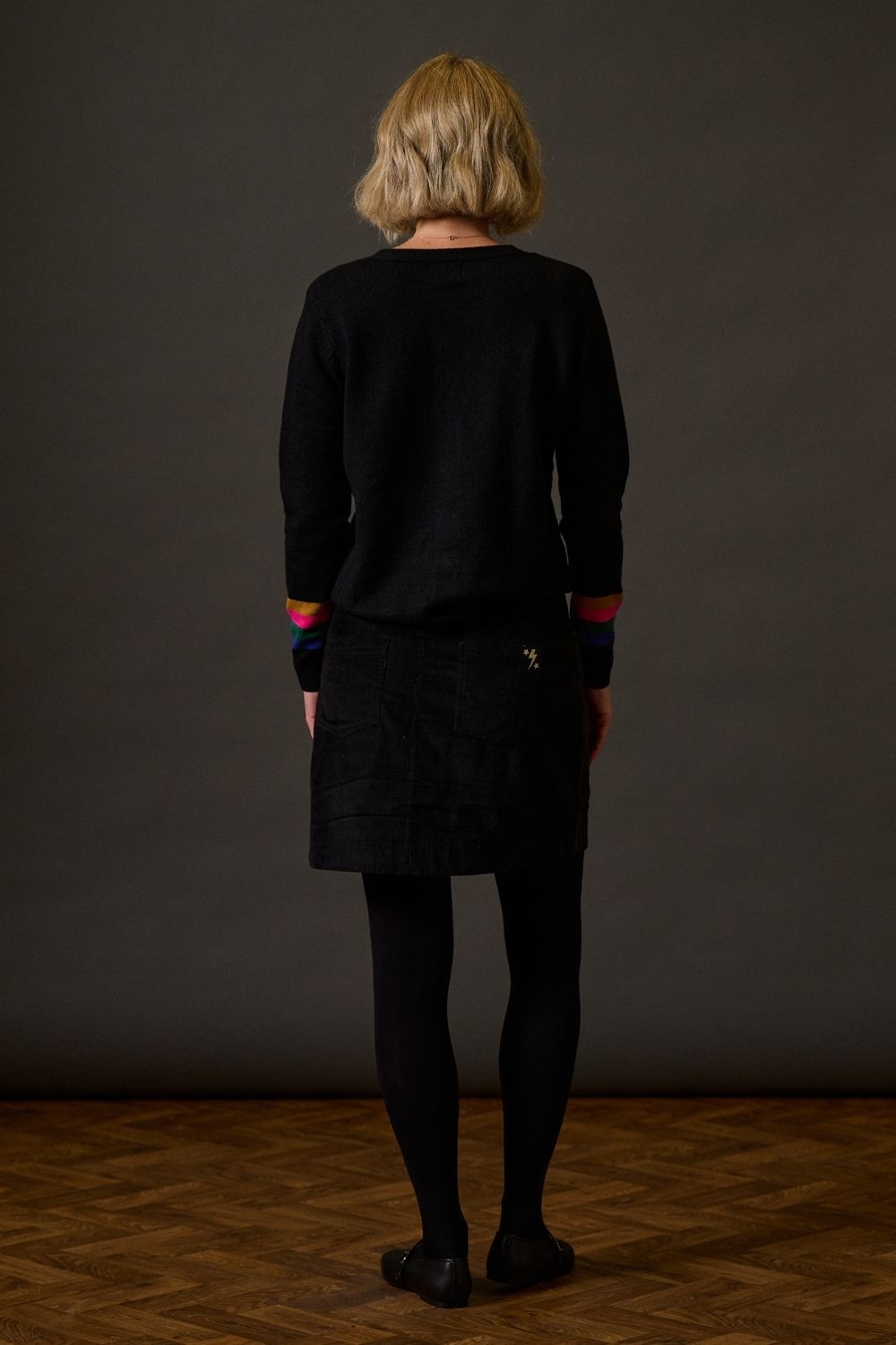 Person wearing a black outfit with colorful cuffs against a dark background