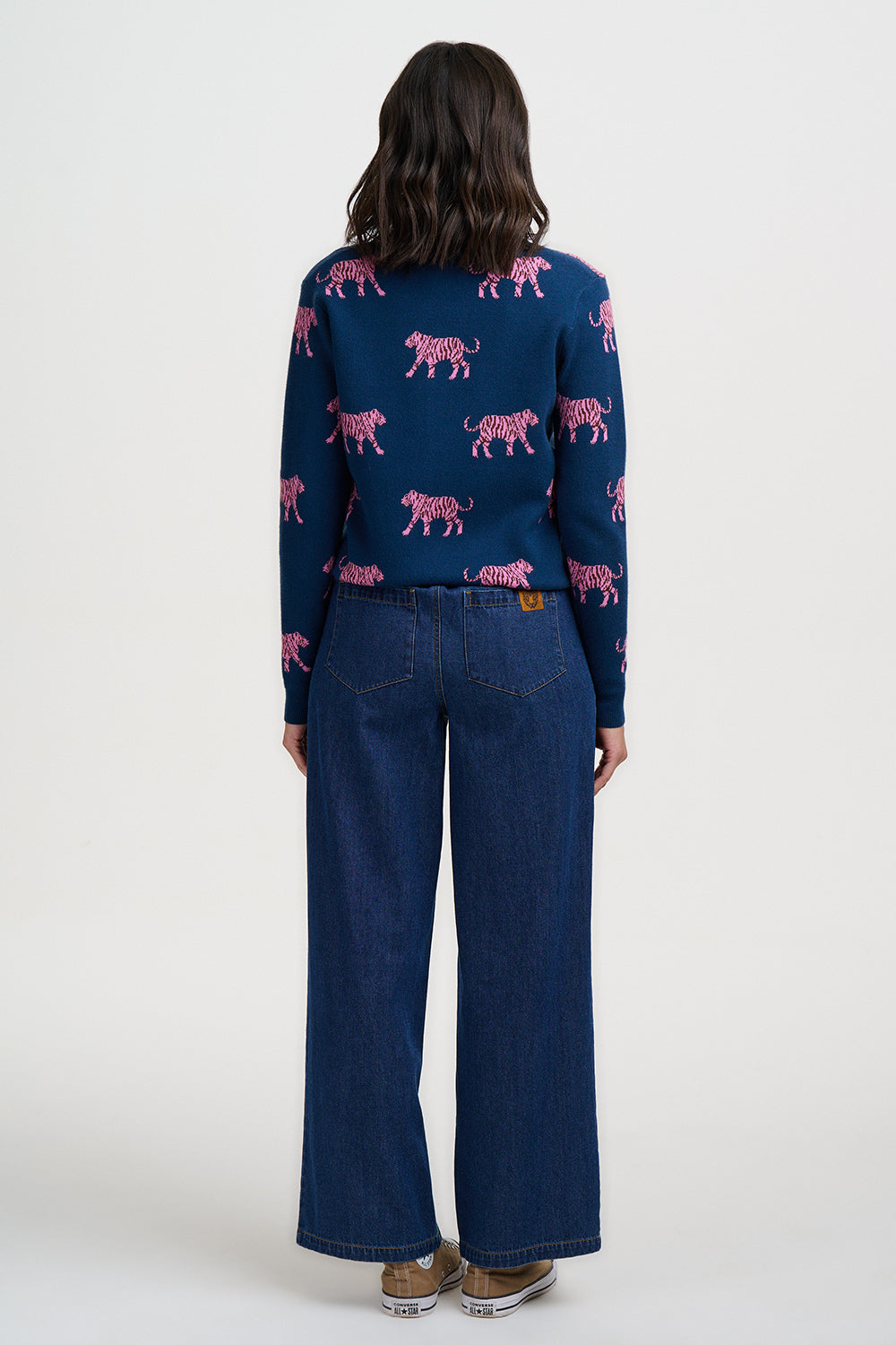 Person wearing a blue sweater with pink tiger pattern and blue jeans on a white background