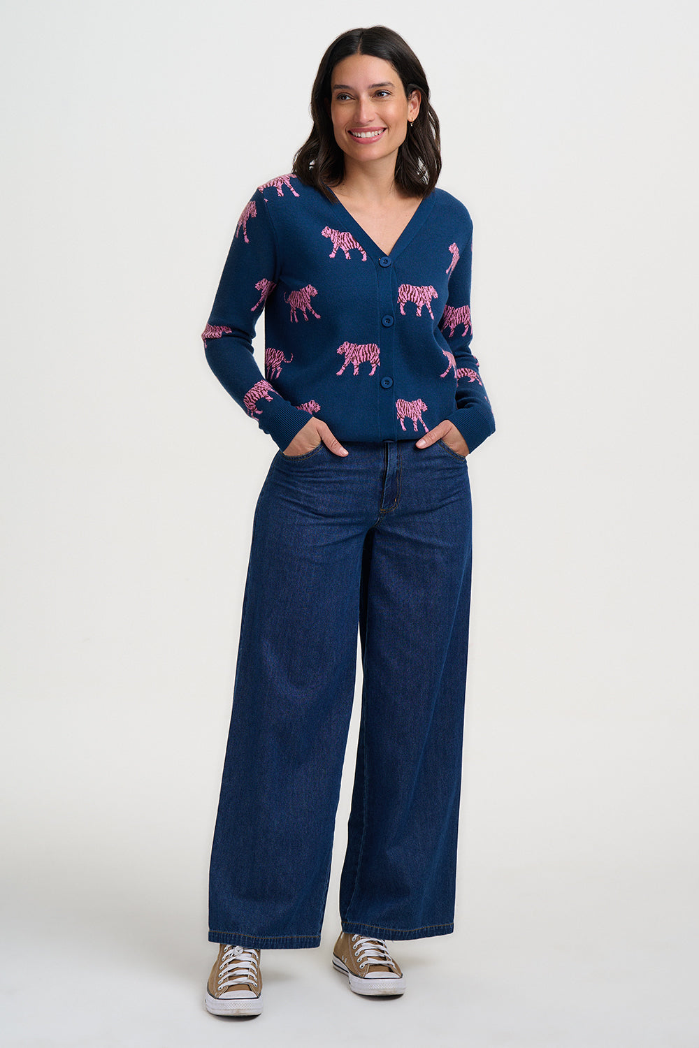 Woman wearing a navy sweater with pink tiger pattern and blue jeans on a white background