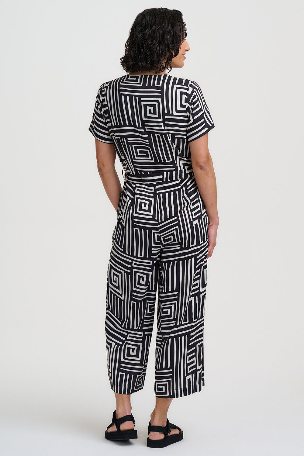 Woman wearing a black and white geometric patterned jumpsuit on a white background