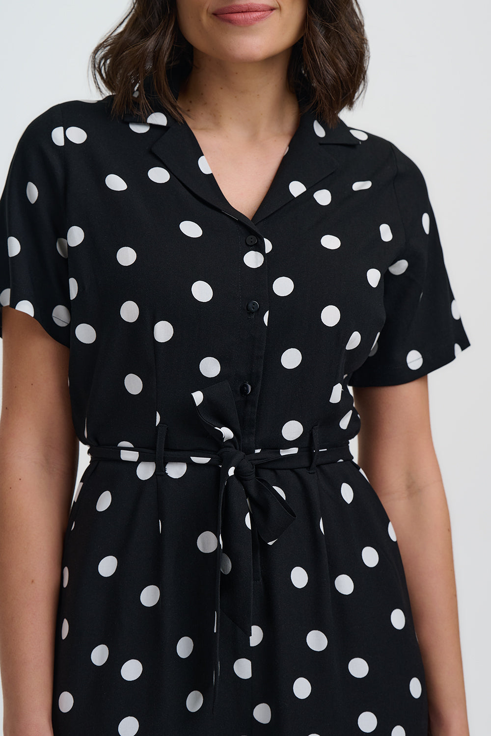 Black dress with white polka dots worn by a model on a white background