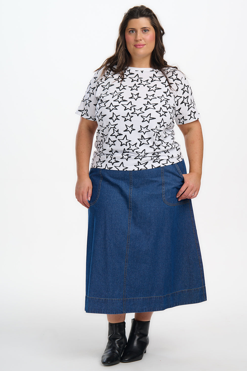 Woman wearing a white t-shirt with black star pattern and a blue denim skirt on a white background