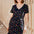 Woman wearing a black dress with colorful patterns and a blue cap, standing against a wooden background.