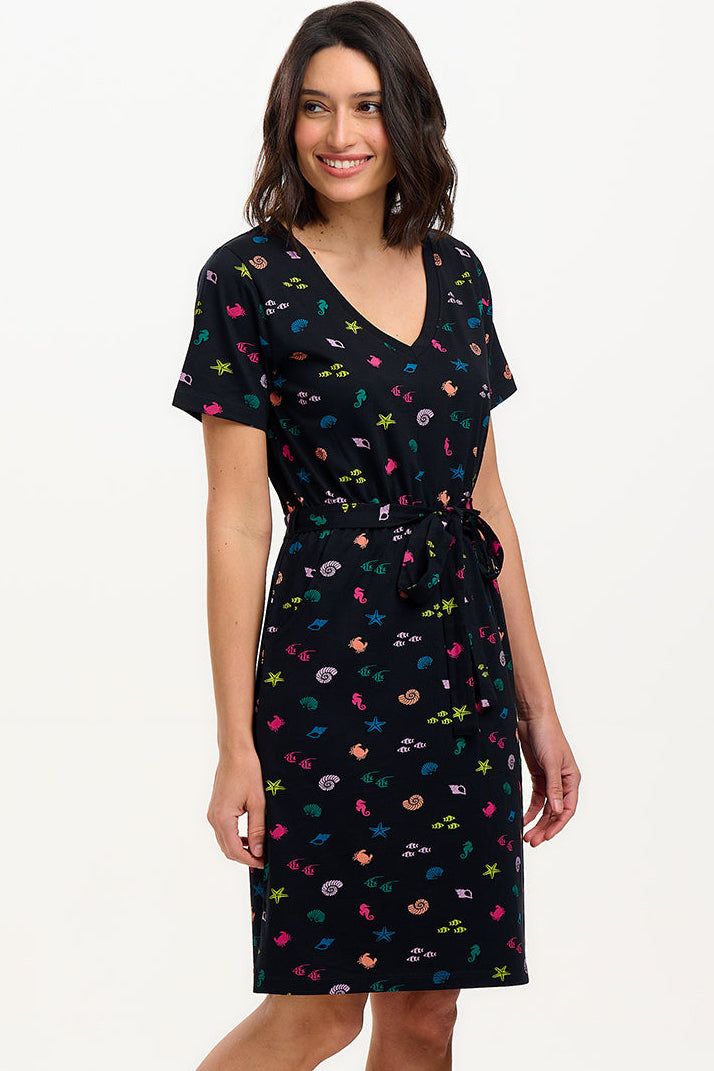 A model wearing a short-sleeved black mini dress with a V-neck, featuring a multicolored underwater theme print. The dress has a matching tie belt and pockets on the skirt.