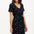 A model wearing a short-sleeved black mini dress with a V-neck, featuring a multicolored underwater theme print. The dress has a matching tie belt and pockets on the skirt.