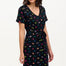 A model wearing a short-sleeved black mini dress with a V-neck, featuring a multicolored underwater theme print. The dress has a matching tie belt and pockets on the skirt.