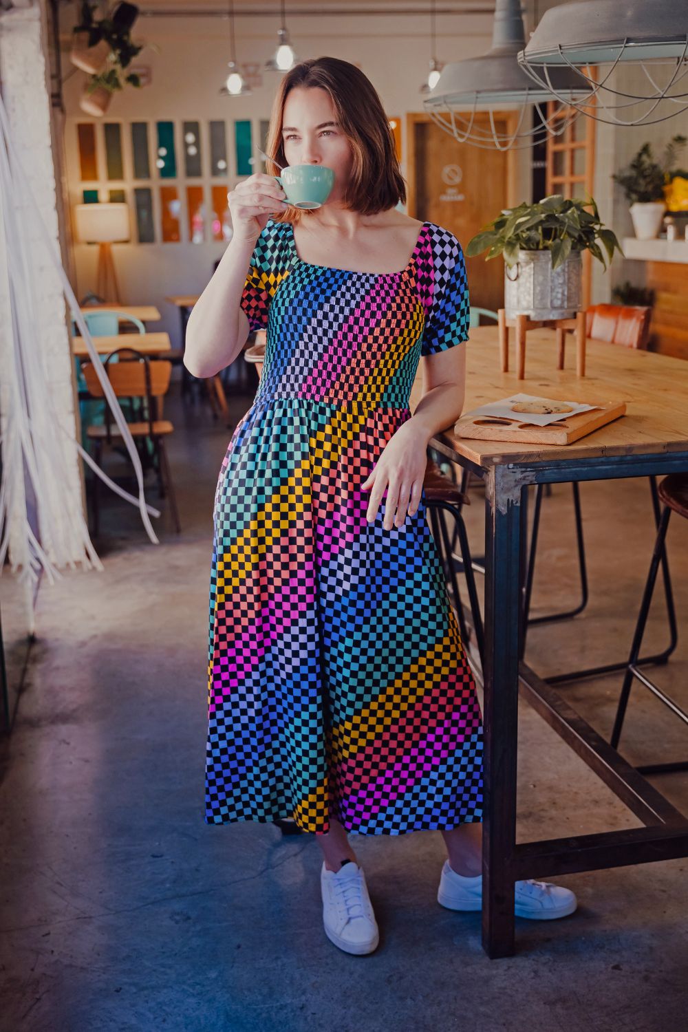 Woman in a colorful dress drinking from a green cup in a cafe.