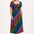 A model wearing a square neckline, short sleeves, high waist, and full midi skirt with pockets, featuring a black base with a multicolored rainbow checkerboard pattern.