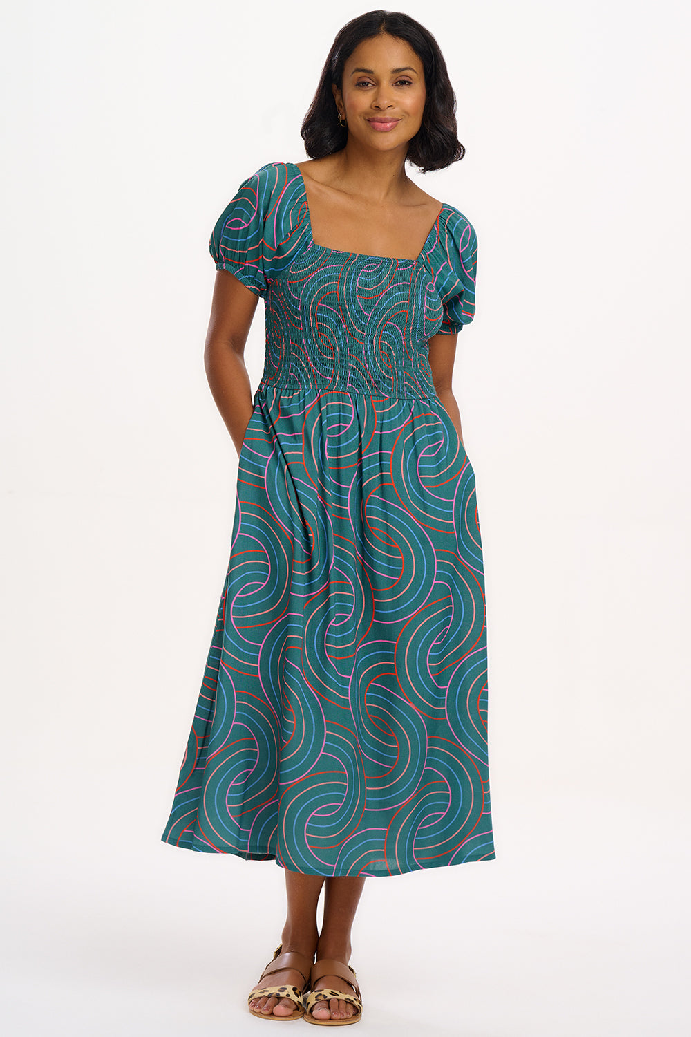 A model wearing a square neckline, short sleeves, and a full midi skirt with a shirred bust, featuring a green base with blue, red, and pink concentric circles pattern.