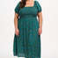 A model wearing a square neckline, short sleeves, and a full midi skirt with a shirred bust, featuring a green base with blue, red, and pink concentric circles pattern.