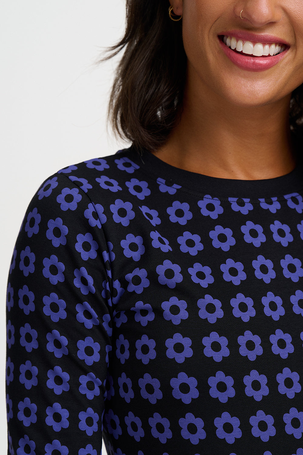 Close-up of a woman wearing a black long-sleeve top with a repeating purple floral pattern, against a plain light background.
