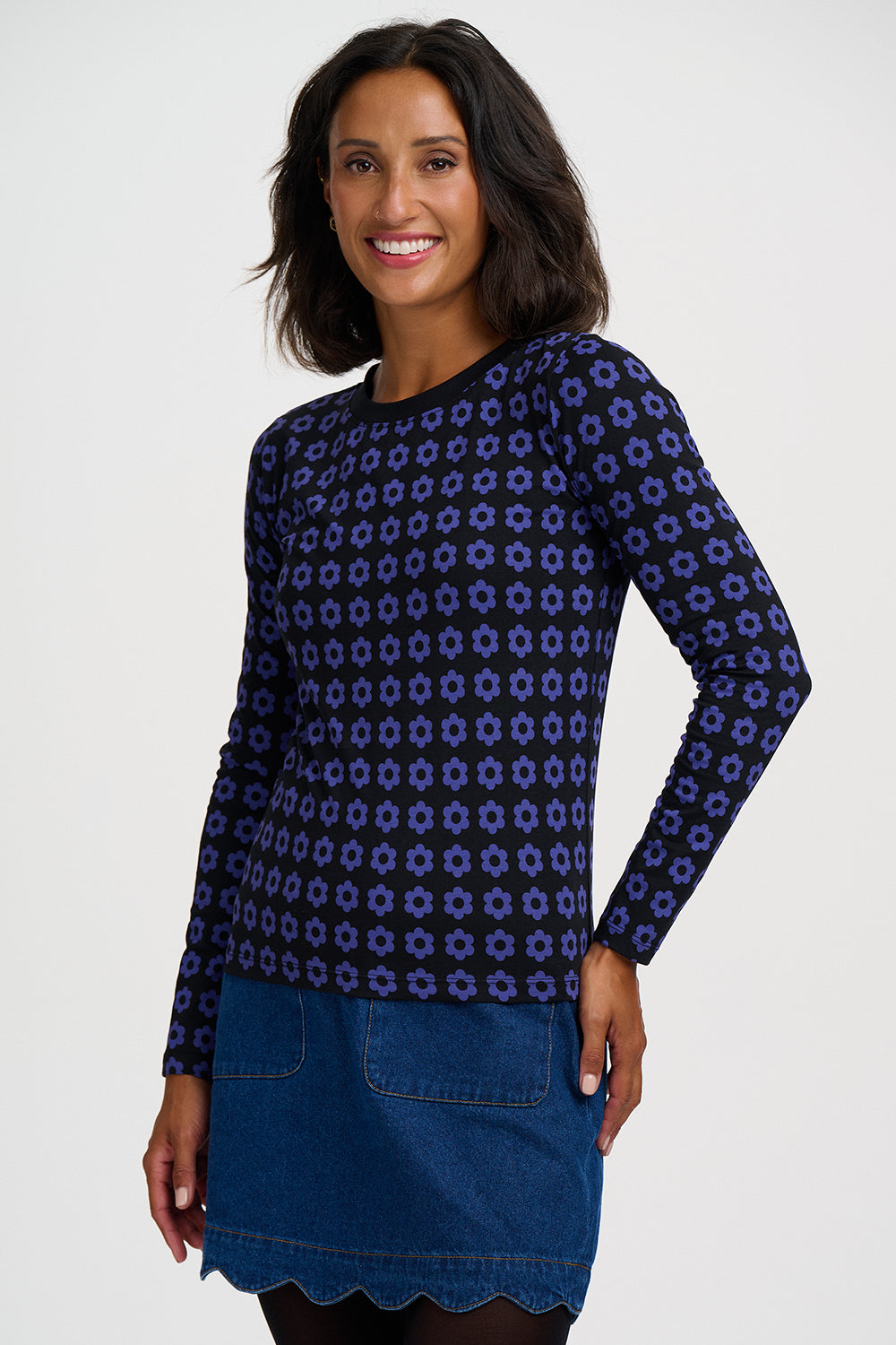 A woman modeling a navy blue long-sleeve knit top with a purple geometric pattern, paired with a blue denim skirt, against a light gray studio background.