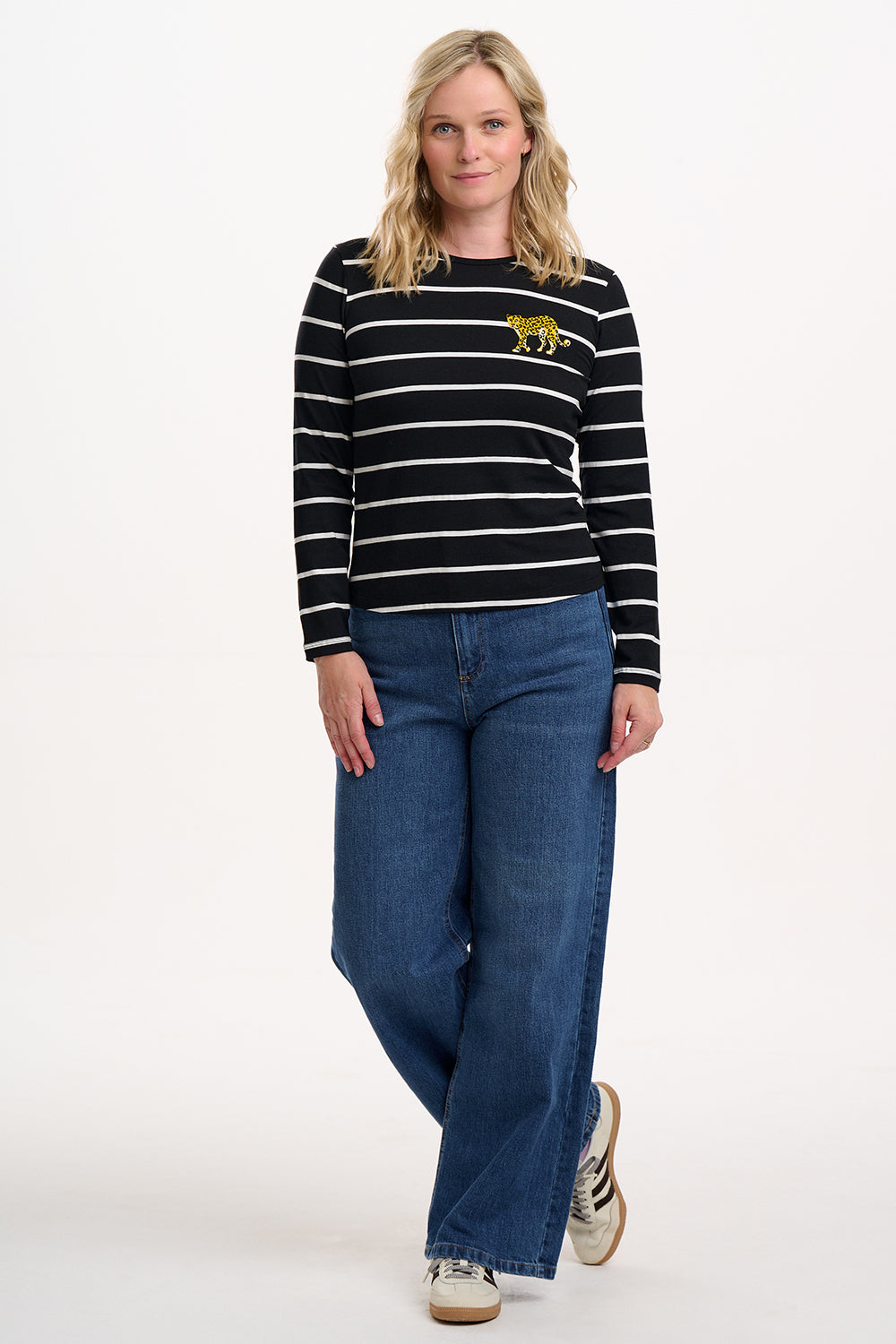 Sugarhill Brighton model wearing a black and white striped sweater with a tiger design and blue jeans on a white background