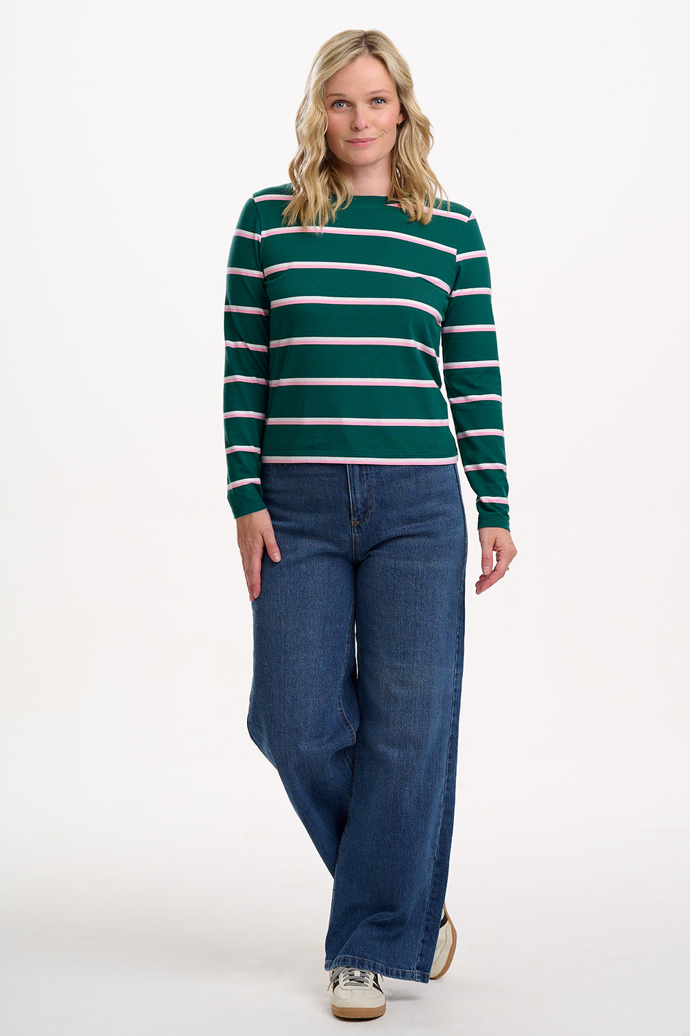 Sugarhill brighton model wearing a green and white striped sweater and blue jeans on a white background
