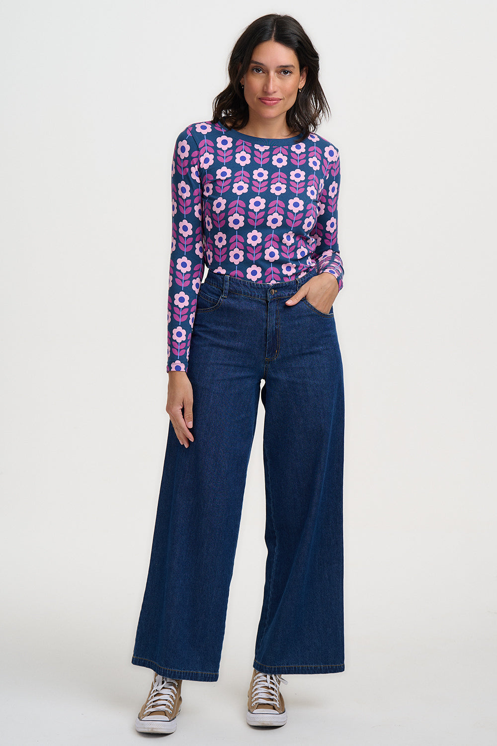 Woman wearing a patterned top and blue jeans on a white background