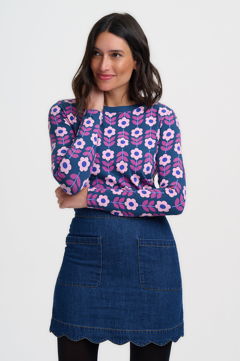 Woman wearing a floral patterned top and denim skirt on a white background