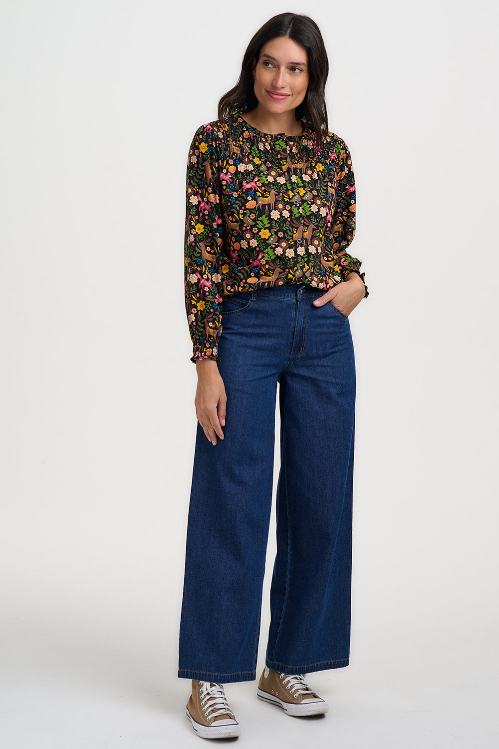Woman wearing a floral blouse and blue jeans on a white background