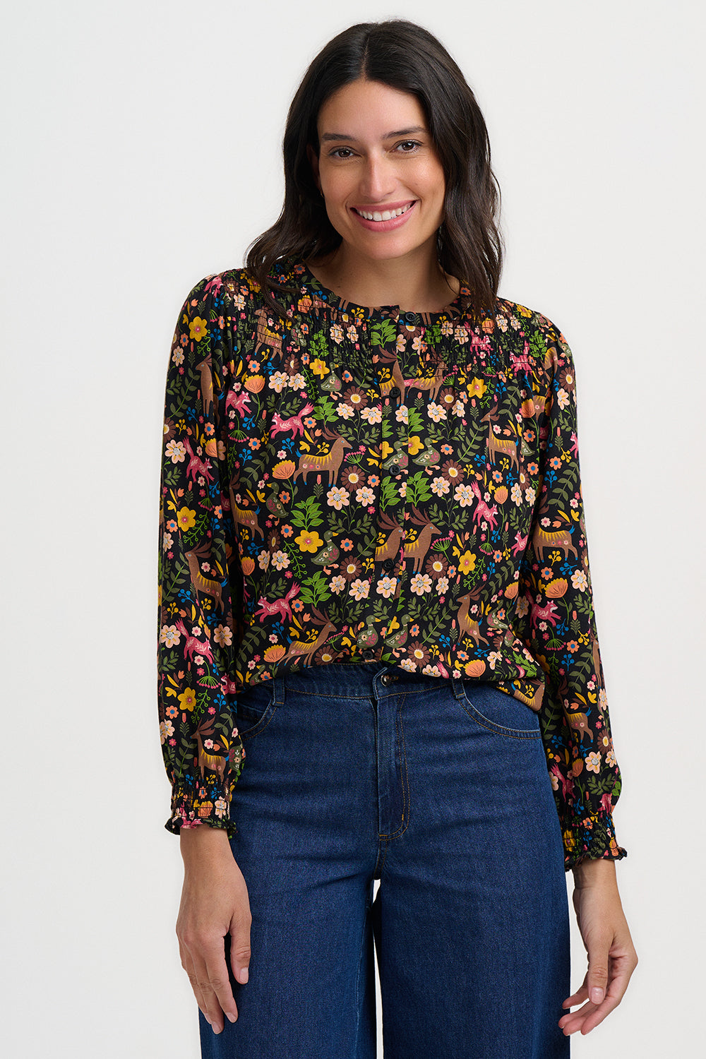 Woman wearing a patterned blouse with long sleeves and blue jeans on a white background