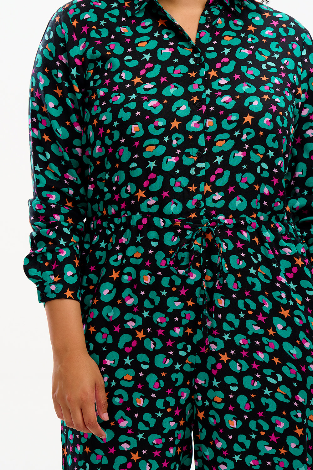 A woman standing, wearing a black and multi-colored floral jumpsuit with full-length sleeves and drawstring waist.