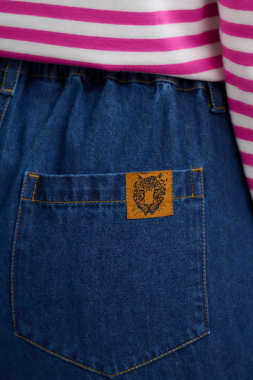 Close-up of a blue denim pocket with a brand logo, wearing a pink and white striped shirt.