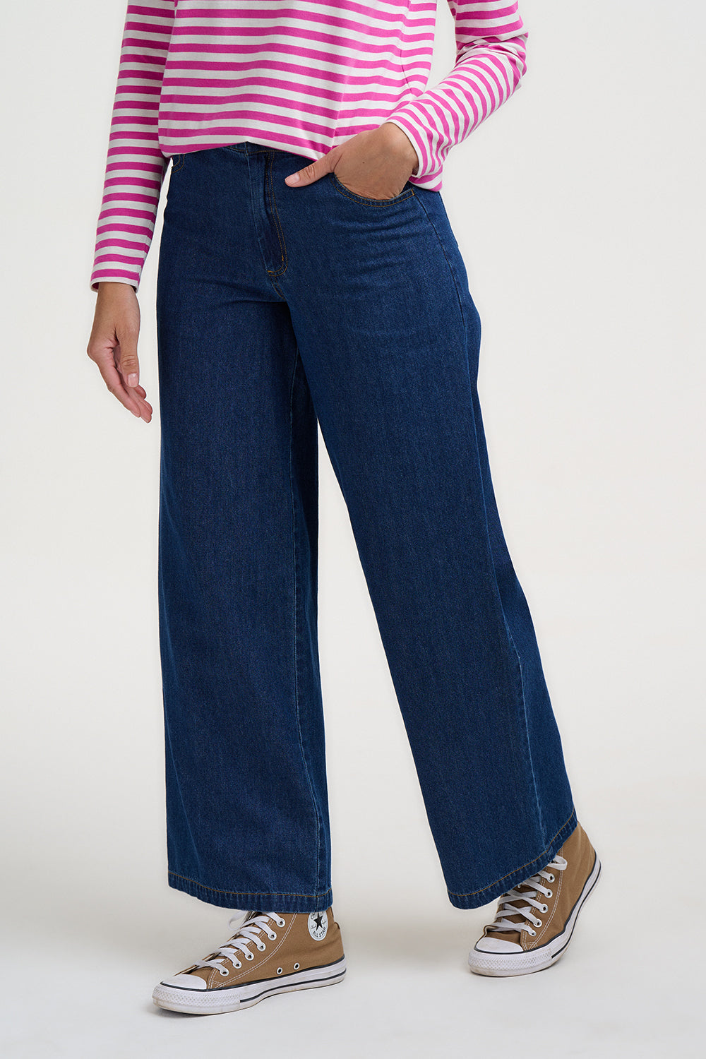 Person wearing a pink and white striped shirt, blue jeans, and brown sneakers on a white background