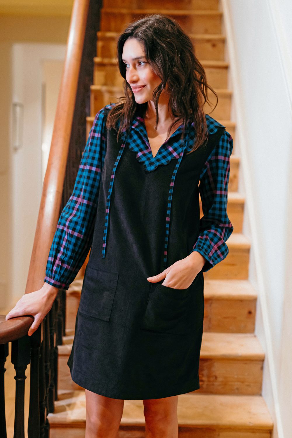 Woman wearing a black dress with plaid trim standing on wooden stairs.