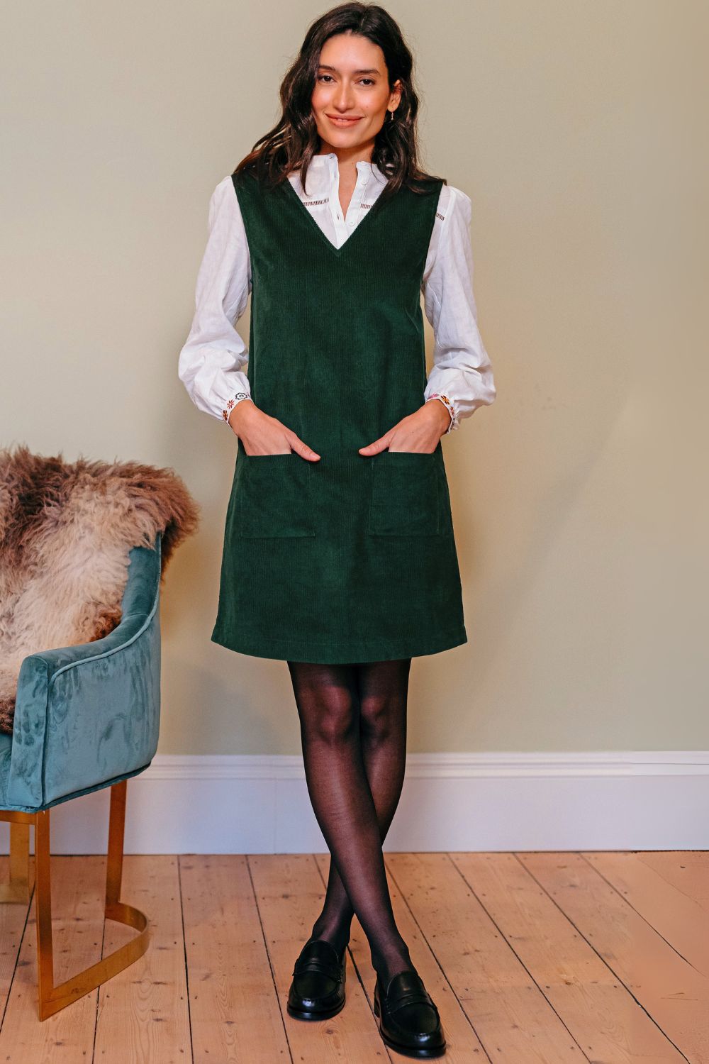 Woman wearing a green dress over a white shirt with a plain background