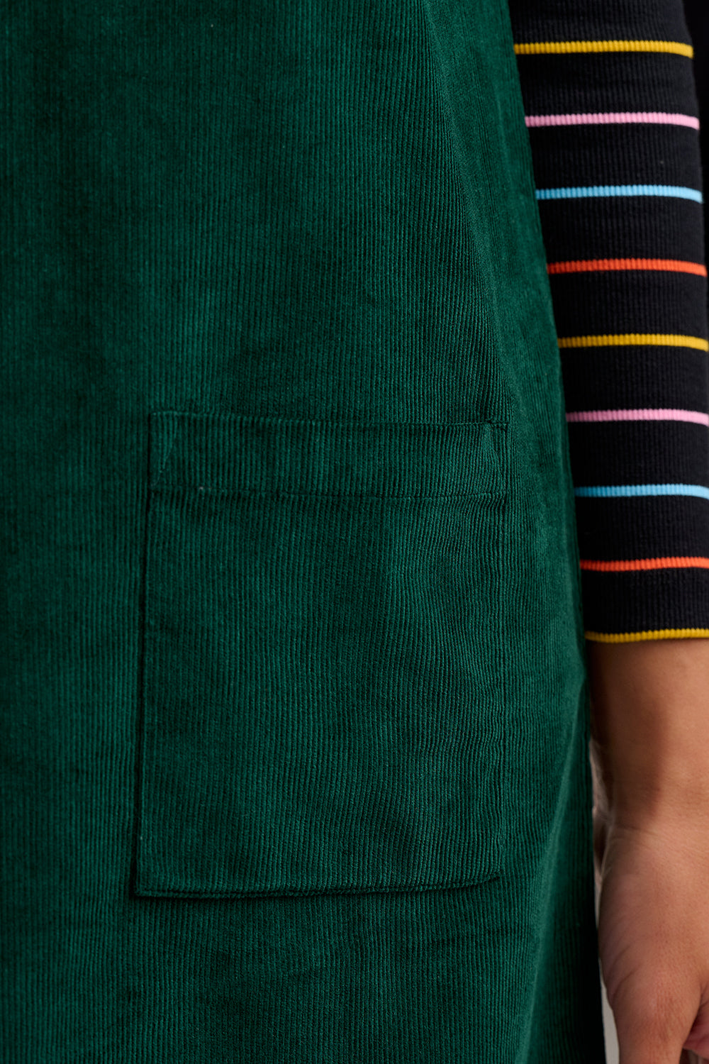 Green apron with a pocket, worn by a person with striped sleeves.