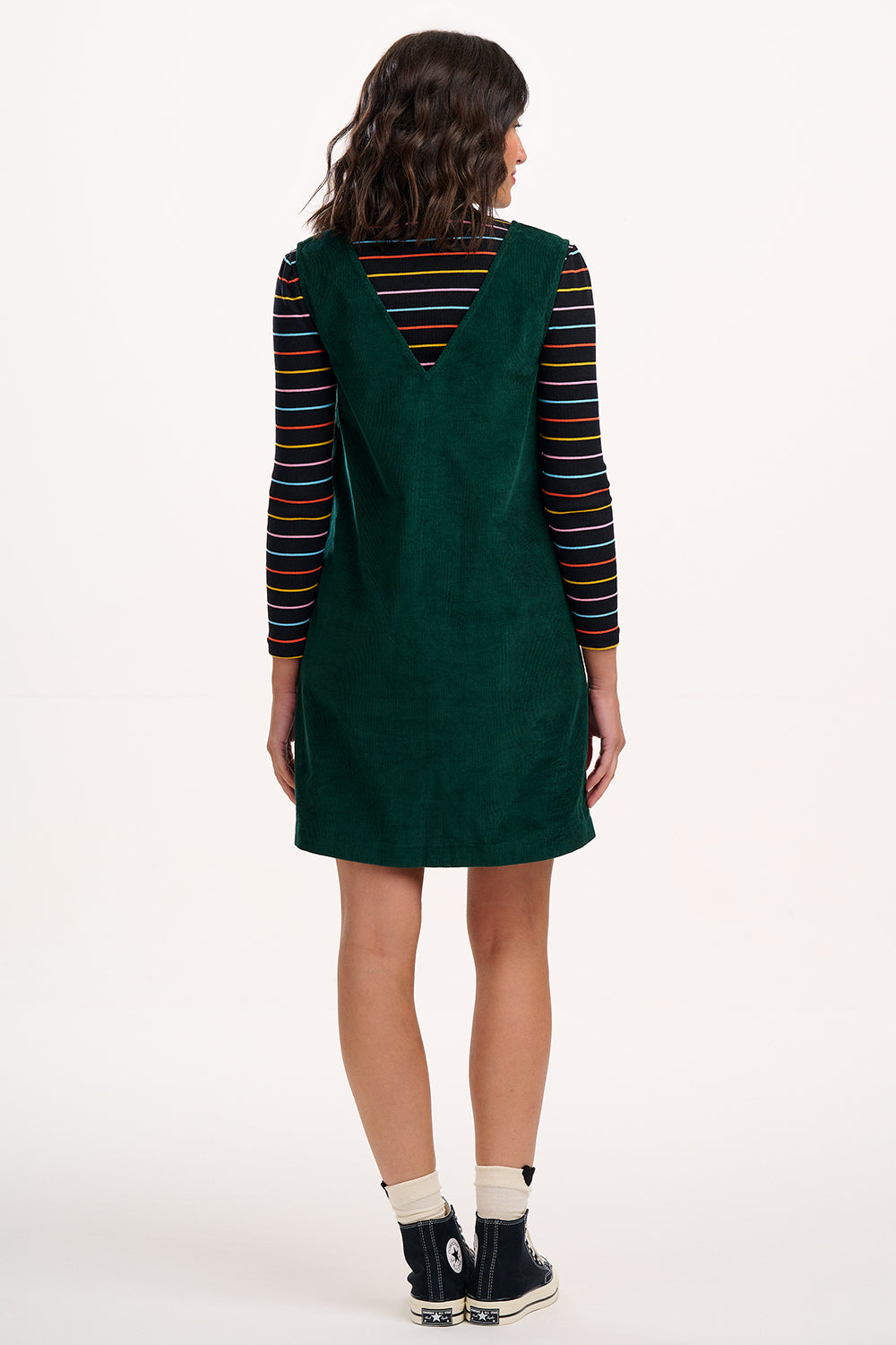 Person wearing a green pinafore dress with a striped shirt underneath on a white background