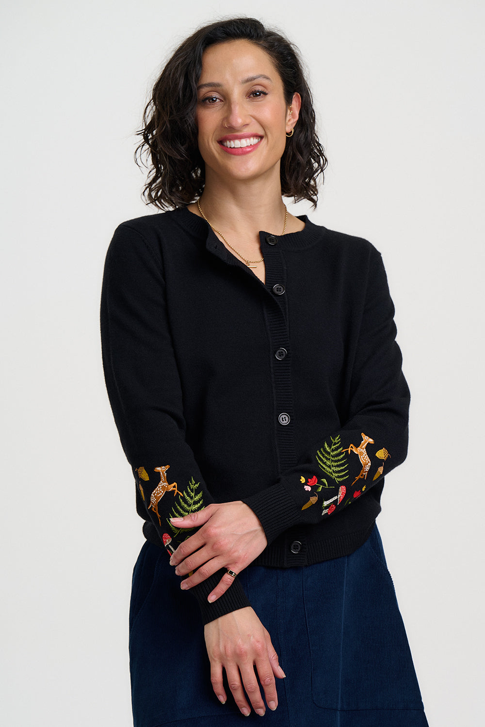 Woman wearing a black cardigan with embroidered designs on a white background