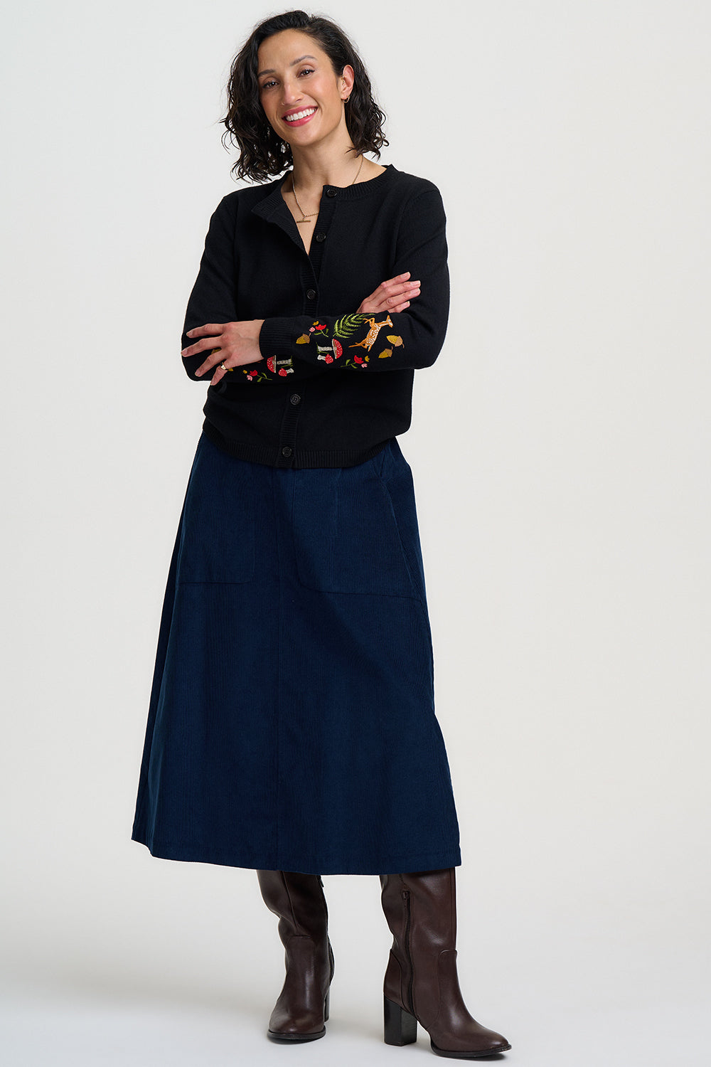 Woman wearing a black blouse with floral embroidery and a navy skirt on a white background