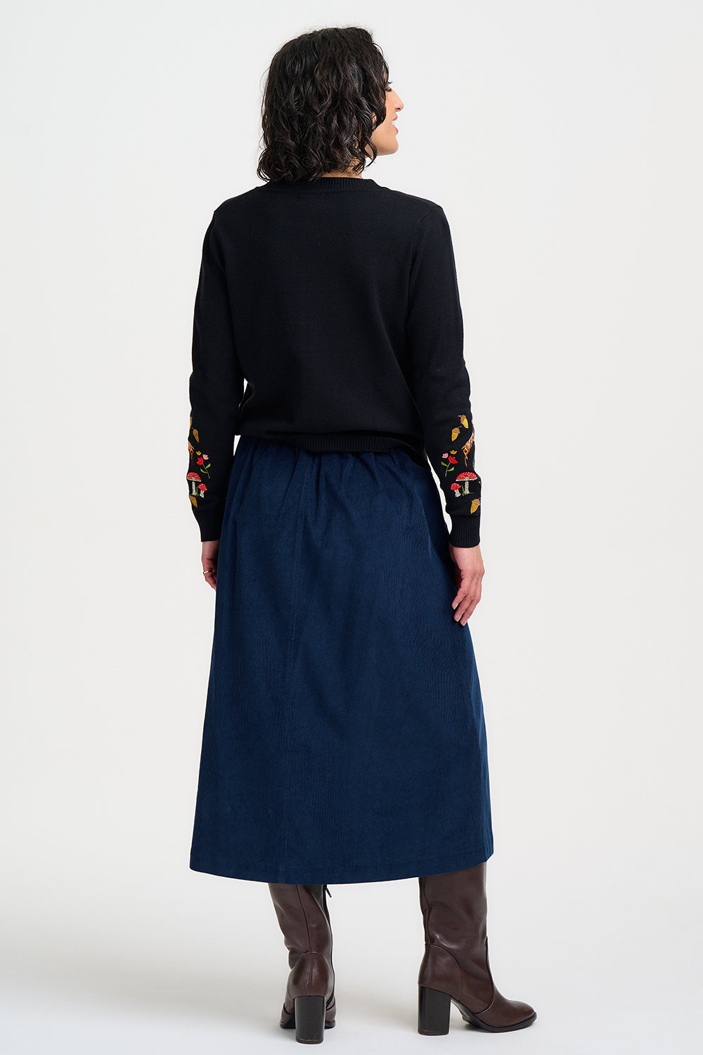 Person wearing a black top with floral embroidery and a navy skirt on a white background