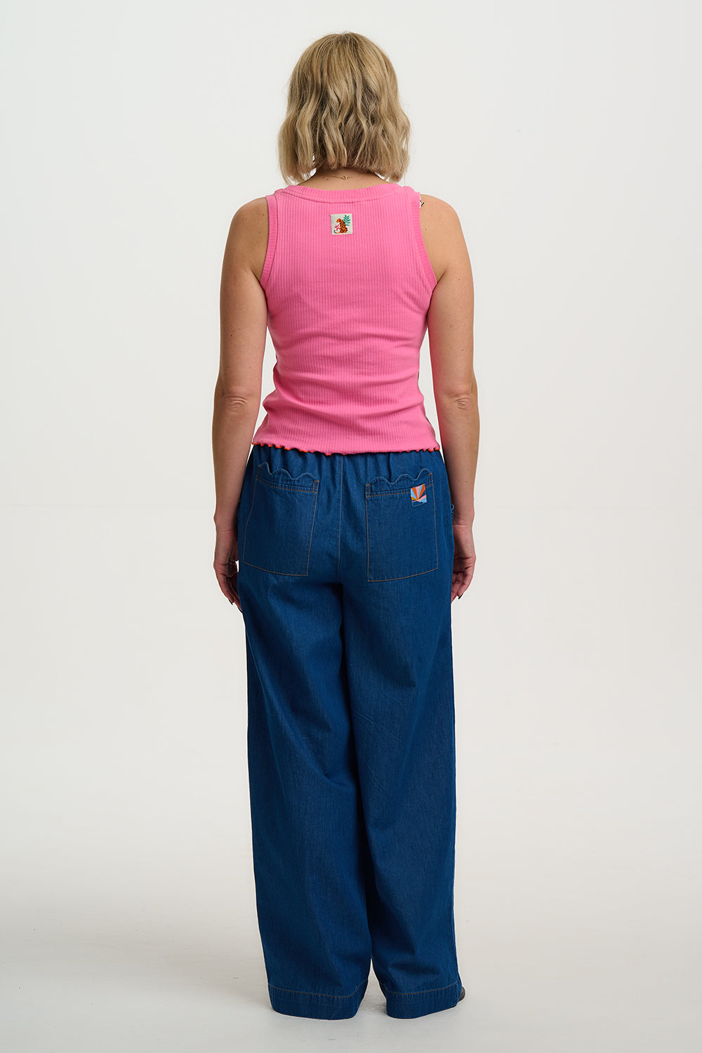 Person wearing a pink sleeveless top and blue pants on a white background