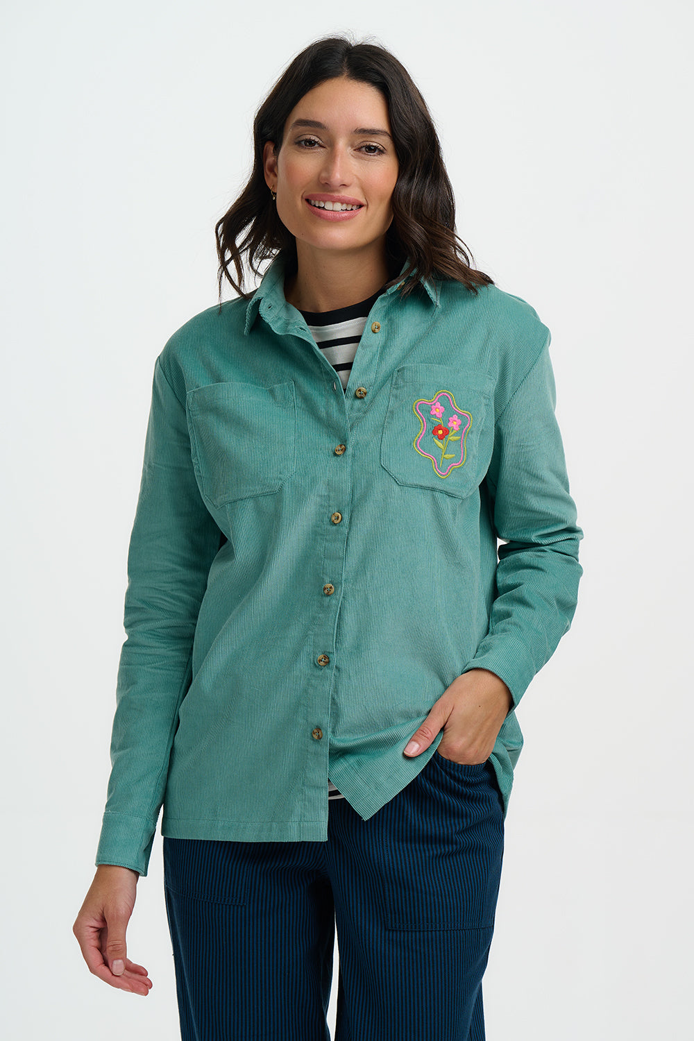 Woman wearing a teal shirt with a floral emblem on a white background
