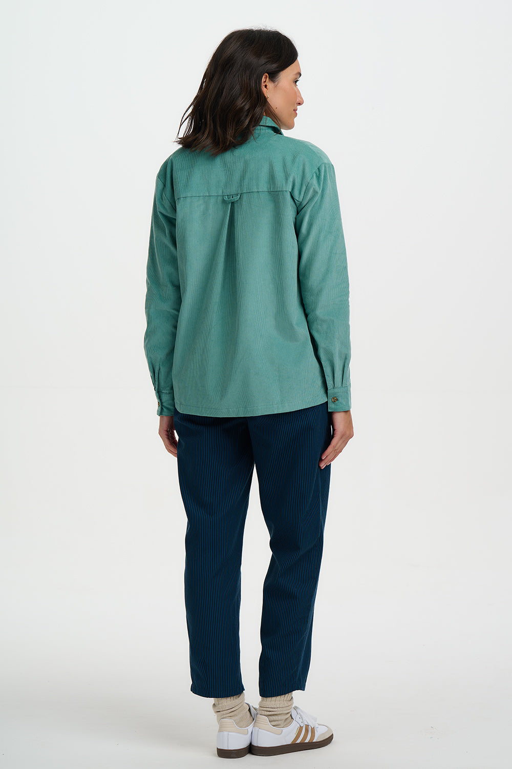 Person wearing a teal shirt and dark pants on a white background