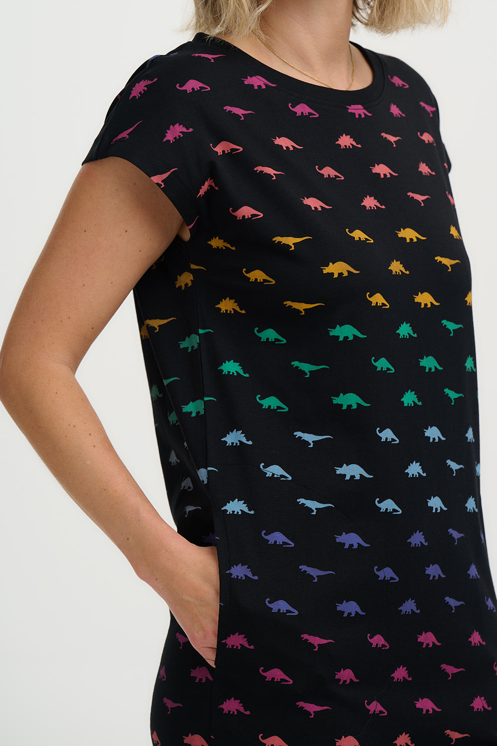Black dress with colorful dinosaur pattern worn by a person on a white background