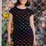 Woman wearing a black dress with colorful patterns in front of a textured wall.