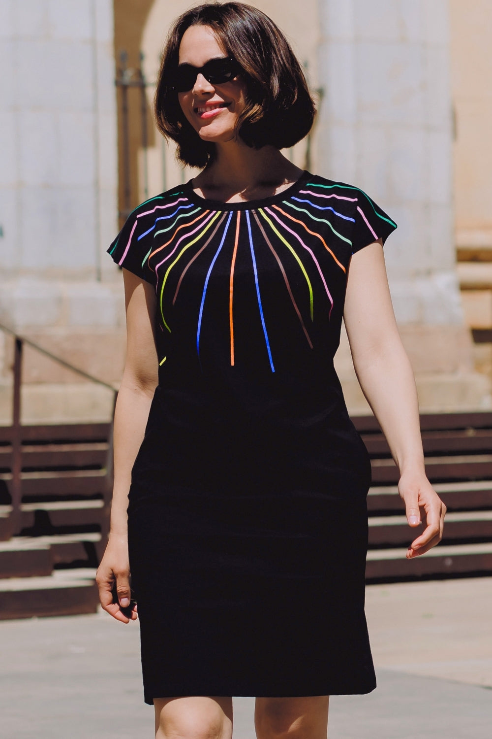 Woman wearing a black dress with colorful striped design outdoors.