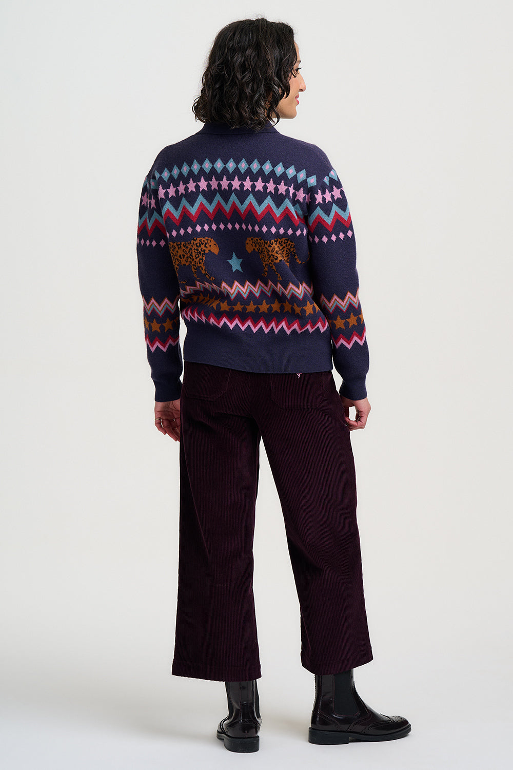 Person wearing a patterned sweater and dark pants on a white background