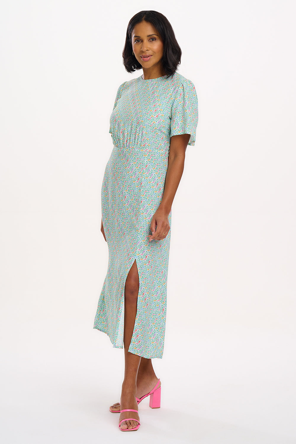A woman standing against a white background wearing an off-white midi tea dress with a Garden Waves print, featuring short fluted sleeves and a slit skirt.