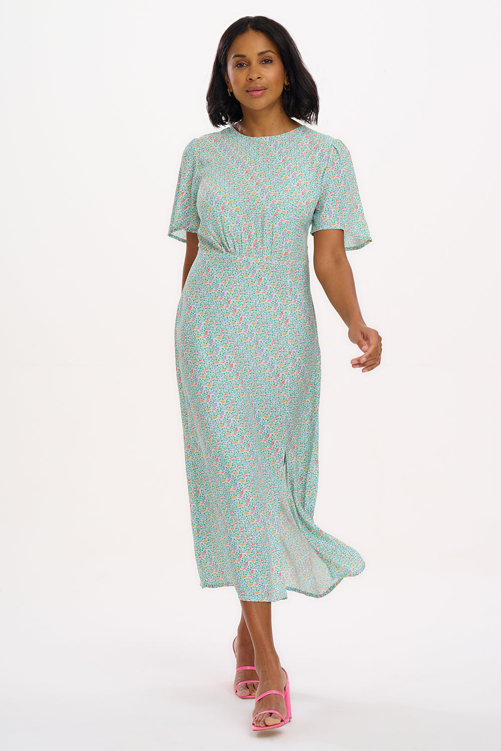 A woman wearing an off-white midi tea dress with a multicolor floral pattern, standing against a white background.
