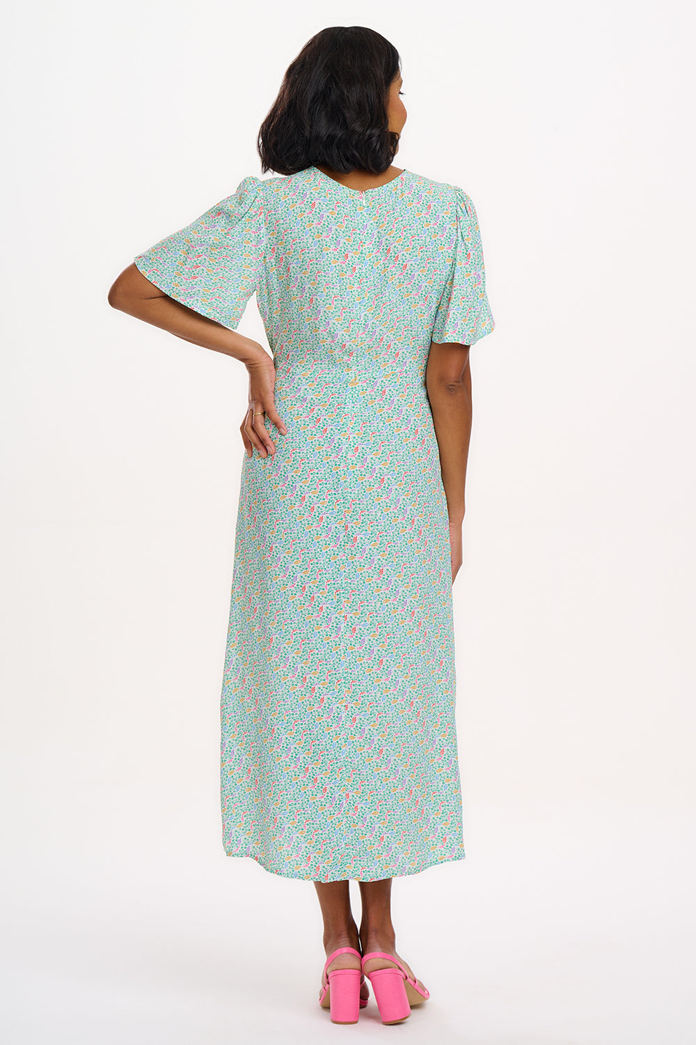 A woman wearing an off-white midi tea dress with a multicolor floral pattern, standing against a white background.