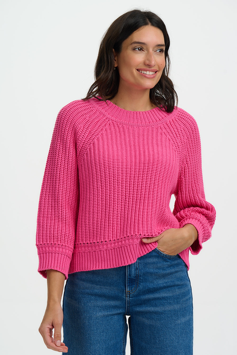 Woman wearing a bright pink sweater and blue jeans on a white background