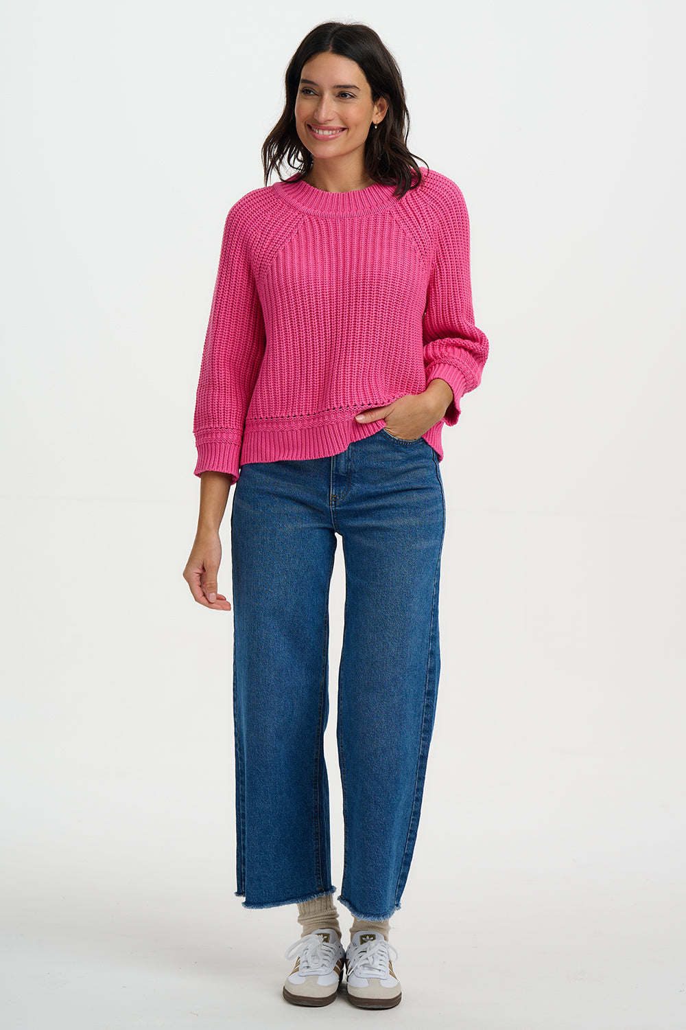 Woman wearing a pink sweater and blue jeans on a white background