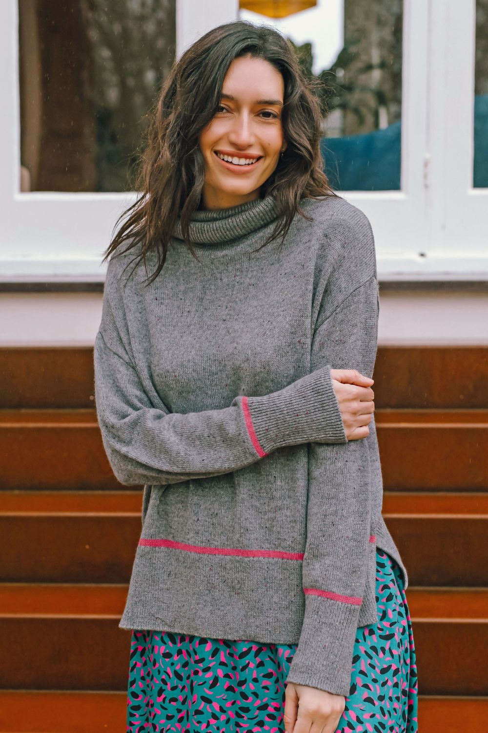 Woman wearing a gray turtleneck sweater with pink accents, standing outdoors.