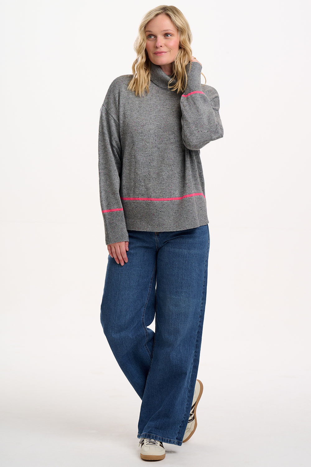Woman wearing a gray sweater with pink accents and blue jeans on a white background