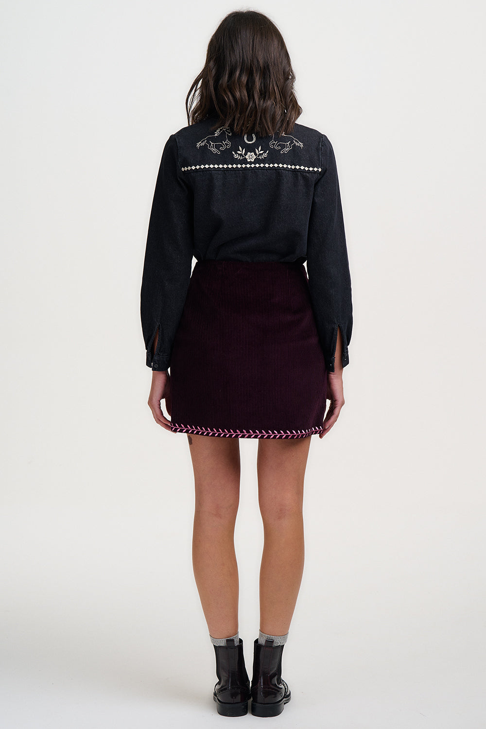 Person wearing a black embroidered shirt and dark purple skirt on a white background