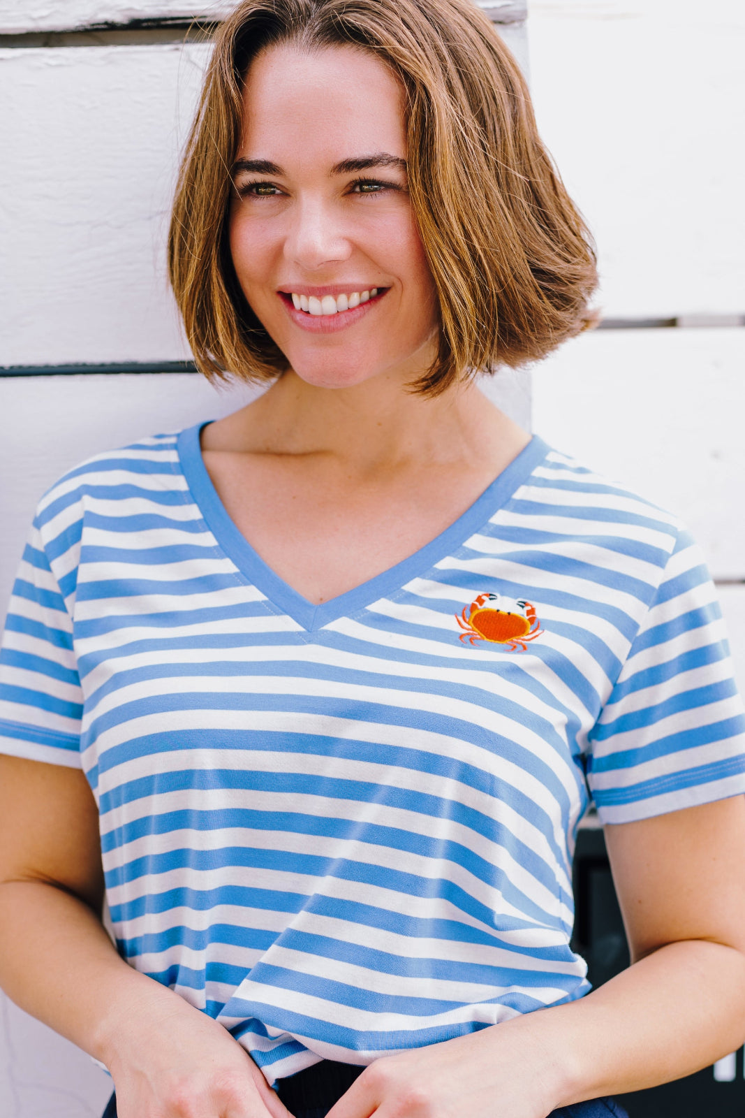 A woman smiling and wearing an off-white and blue striped t-shirt with a deep v-neckline and a small graphic on the chest.