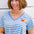 A woman smiling and wearing an off-white and blue striped t-shirt with a deep v-neckline and a small graphic on the chest.